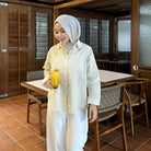 Woman wearing light yellow striped shirt by Renaette holding a glass of orange juice in a restaurant setting