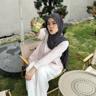 Woman in pink striped shirt by Renaette sitting outdoors holding a green cup, with a casual setting in the background.