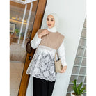 A modest woman wearing a beige and white vest by Abame with floral lace detail, paired with black pants and a white hijab, carrying a small beige handbag.