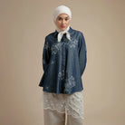 Woman wearing a dark denim shirt by Hijabchic with floral embroidery and a white hijab on a beige background