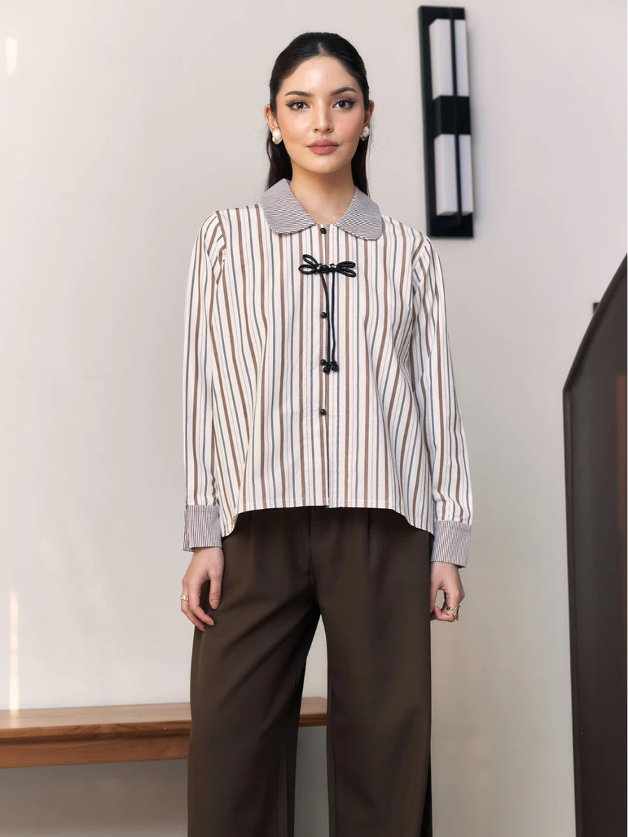Woman wearing a striped shirt with a collar by Studio Tui and brown pants in an indoor setting.