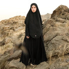 A woman wearing a black Lozy Hijab abaya, standing against a neutral background with decorative candles to the side.