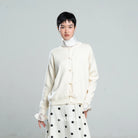 Person wearing a white cardigan by BWBYAZ with a polka dot skirt on a gray background