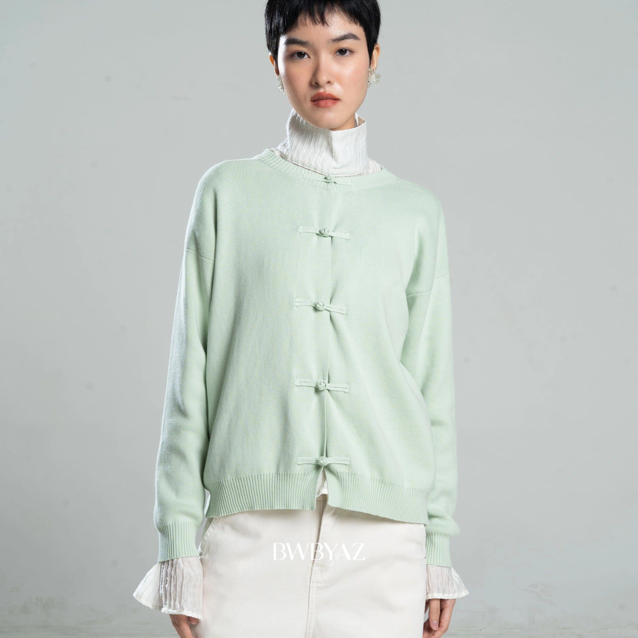 Person wearing a light green cardigan by BWBYAZ over a white turtleneck on a gray background