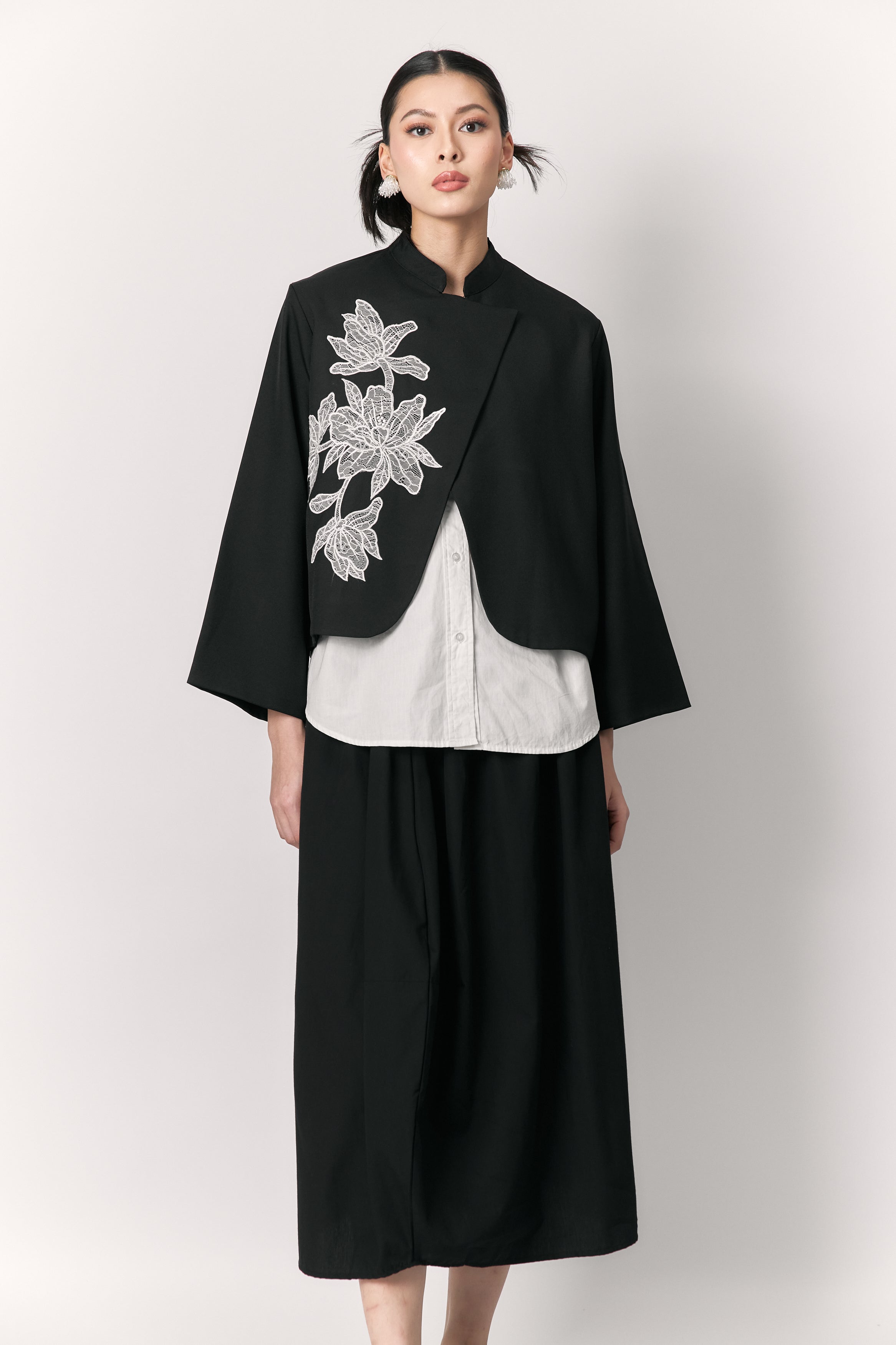 Woman wearing a black outer with floral embroidery by Studio Tui on a white background