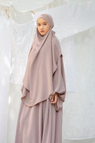 A woman wearing a grey cream abaya set with a matching headscarf by Lozy Hijab, standing indoors.