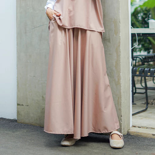 Person wearing a long pink skirt by Abame standing against a wall.