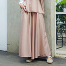 Person wearing a long pink skirt by Abame standing against a wall.