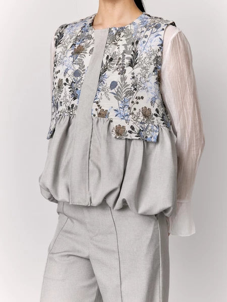 Person wearing a grey vest with floral details by Studio Tui on a plain background