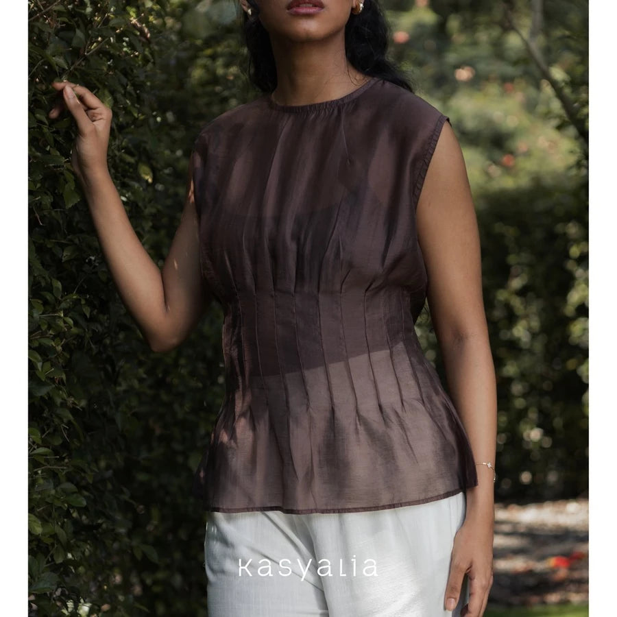 Woman wearing a brown top and white pants standing in front of green foliage, with 'kasyalia' branding.