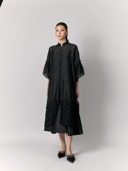 Woman wearing a black tunic by Studio Tui with sheer sleeves against a white background