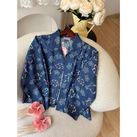 Blue floral-patterned denim jacket from Haidee Orlin on a chair with pink slippers and flowers in the background