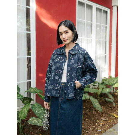 Woman wearing a Dark blue floral-patterned denim jacket from Haidee Orlin in front of a red wall with white trim.