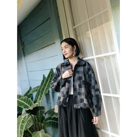 Woman wearing a black checkered denim jacket from Haidee Orlin standing in front of a building with plants around.