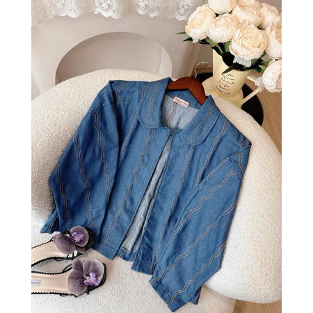 Blue denim jacket with a wavy pattern from Haidee Orlin on a chair with flowers and shoes in the background