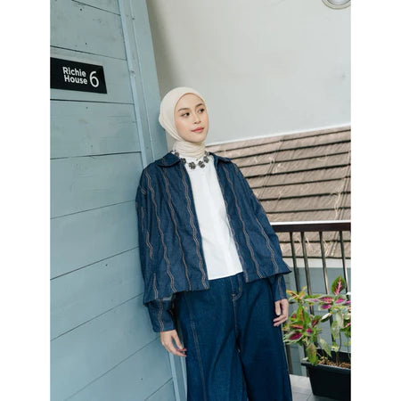Woman wearing a dark blue denim jacket with wave pattern from Haidee Orlin and white hijab standing against a building with 'Richie House 6' sign.