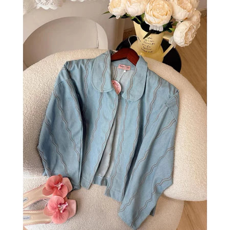 Light blue denim jacket with wave pattern from Haidee Orlin on a chair with a vase of flowers in the background