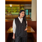Woman in a patterned black vest over a white shirt standing in a restaurant setting