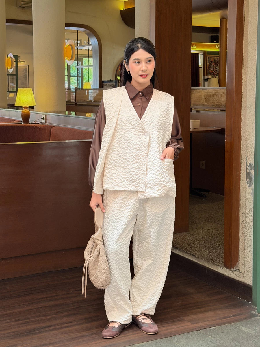 Person wearing a brown shirt with a broken white vest and pants in an indoor setting.