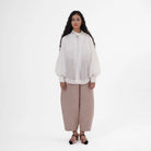 Woman wearing a white outer by Jenna & Kaia and beige pants on a white background