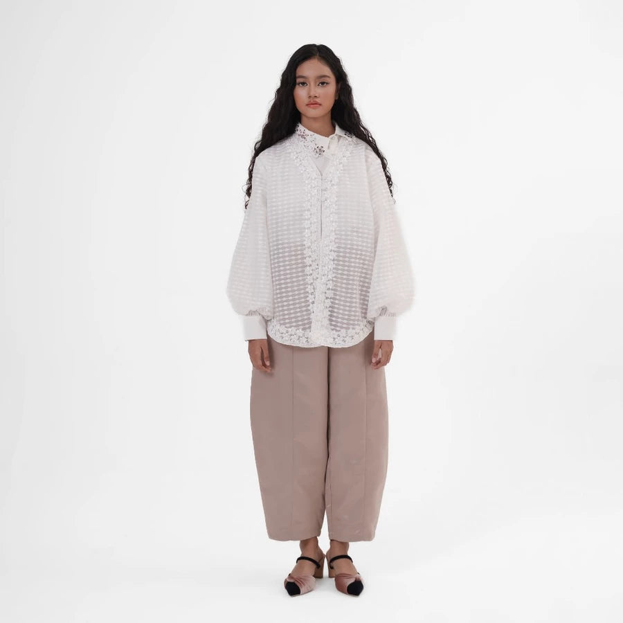 Woman wearing a white outer by Jenna & Kaia and beige pants on a white background