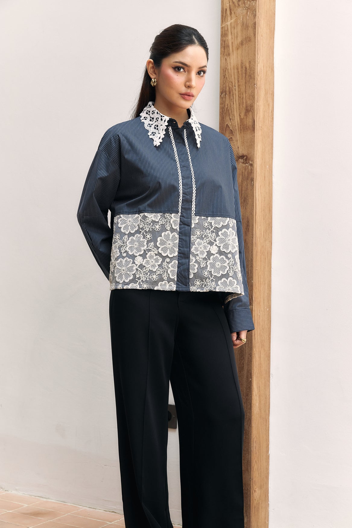 Woman wearing a navy shirt with white lace details by Studio Tui against a neutral background