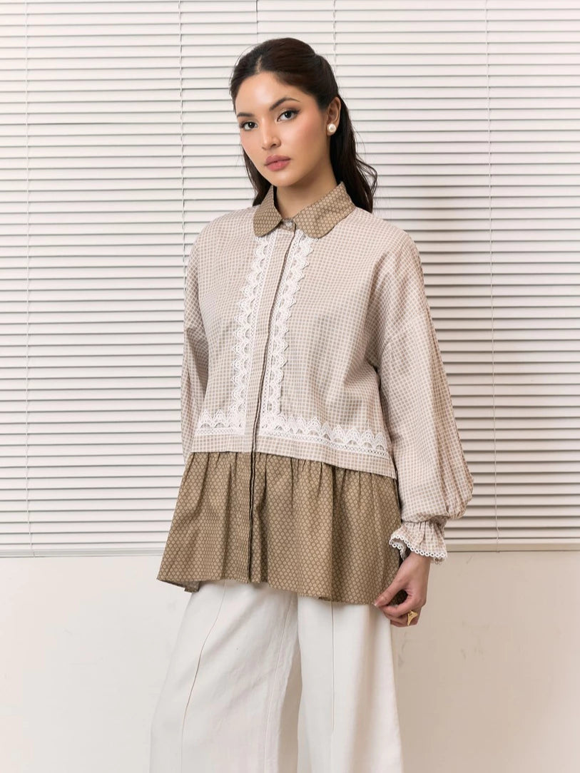 A woman models a beige and brown patterned shirt by Studio Tui with white lace trim and white wide-leg pants, standing in front of white window blinds.