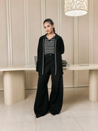 Woman in black cardigan by Studio Tui over a striped polos standing in a modern interior setting
