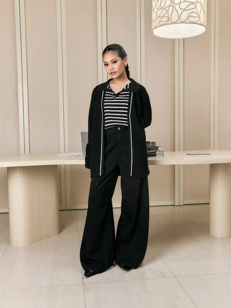 Woman in black cardigan by Studio Tui over a striped polos standing in a modern interior setting