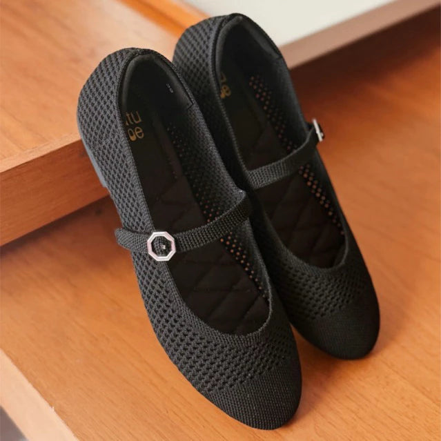 Pair of black mesh flatshoes with a strap by Tutu Toe on a wooden floor