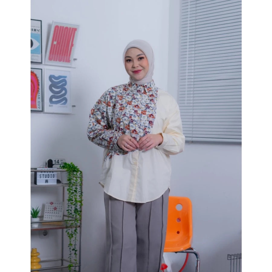 Woman wearing a floral shirt by Abame over a white shirt with gray pants in an office setting.