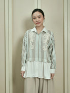 Woman wearing a striped shirt by Studio Tui with floral embroidery against a plain background