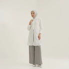 Seorang wanita menggunakan Mosa Tuniq, sebuah premium tunik dengan material cotton embroidery dan terdapat pita belakang yang bisa disesuaikan dengan badan, dari brand Tunique