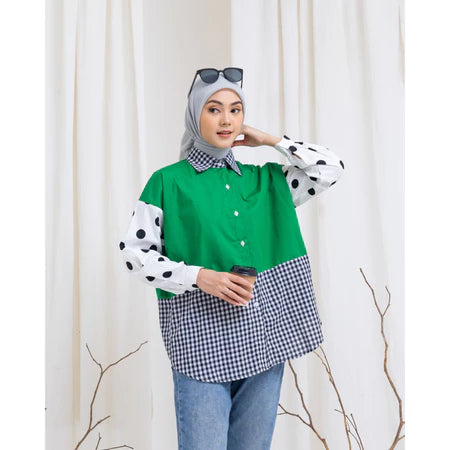 Woman wearing a green, polka dot, and checkered shirt by Abame against a white curtain background