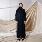 Woman wearing a black abaya one set by Tubita against a draped fabric background
