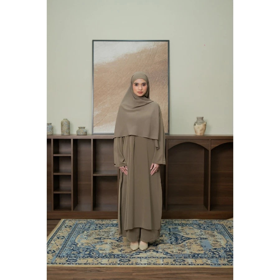 Woman in a beige outfit set by Tubita standing in a room with wooden shelves and a framed picture on the wall.