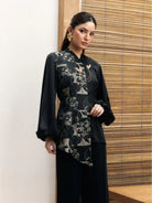 Woman wearing a black floral longsleeves blouse by Studio Tui against a wooden panel background