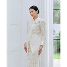 Woman wearing a ivory white lace blouse by Kasa Heritage standing in a room with white walls and a window.
