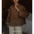Person wearing a brown button-up shirt with a blurred background, featuring the brand 'kasyalia'.
