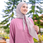 Woman wearing a pink shirt and gray pashmina hijab by Puru Kambera with greenery in the background