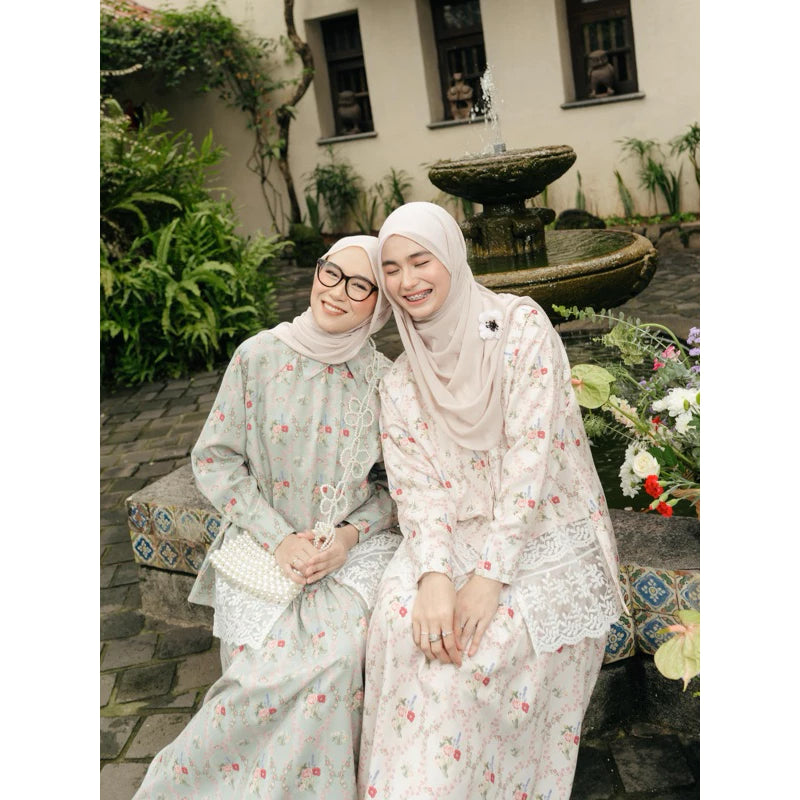 Two women in floral dresses and Narnia Skirt from Haidee Orlin sitting together in a garden with a fountain in the background.