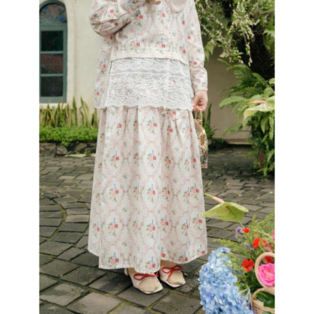Person wearing a cream floral dress and skirt from Haidee Orlin standing outdoors on a stone path with plants and flowers.