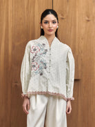 Woman wearing a white embroidered blouse with floral patterns by Studio Tui against a wooden background