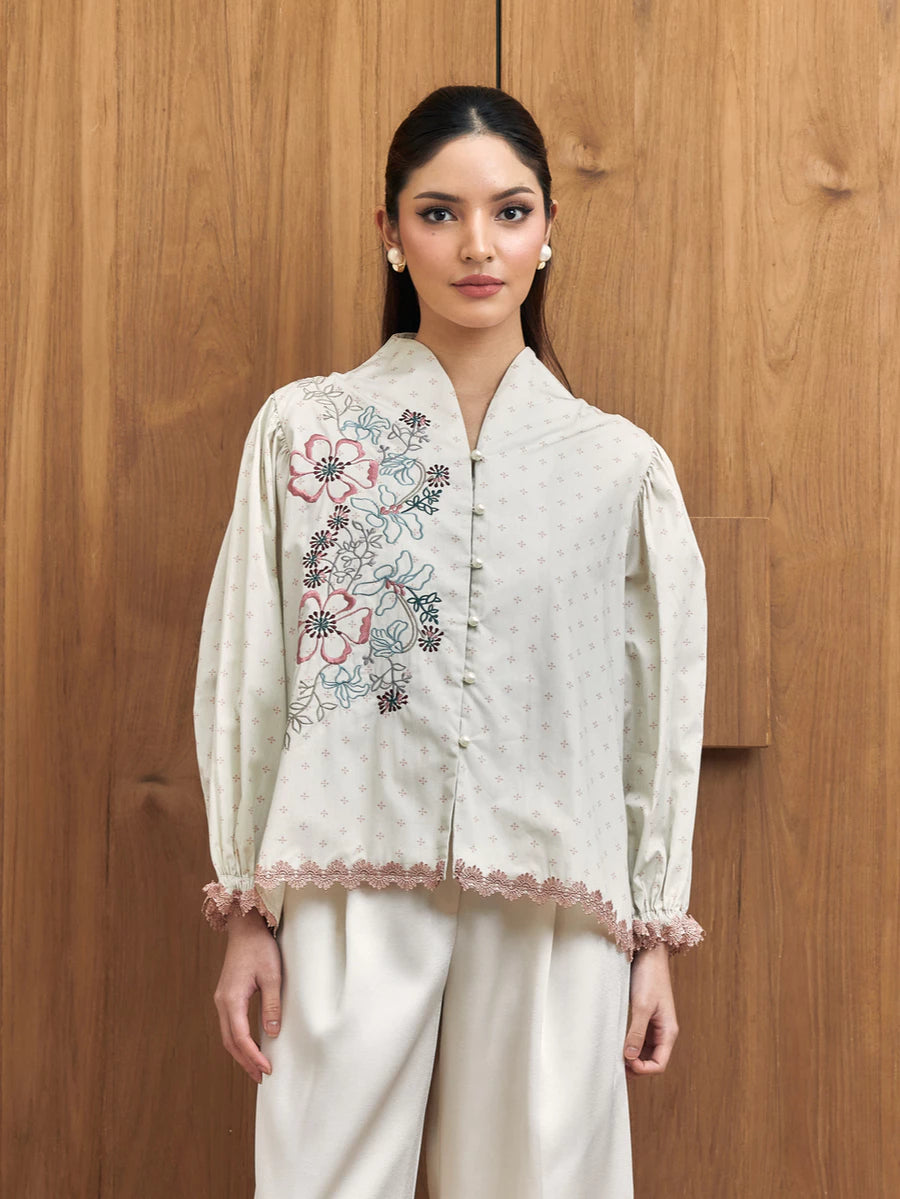 Woman wearing a white embroidered blouse with floral patterns by Studio Tui against a wooden background
