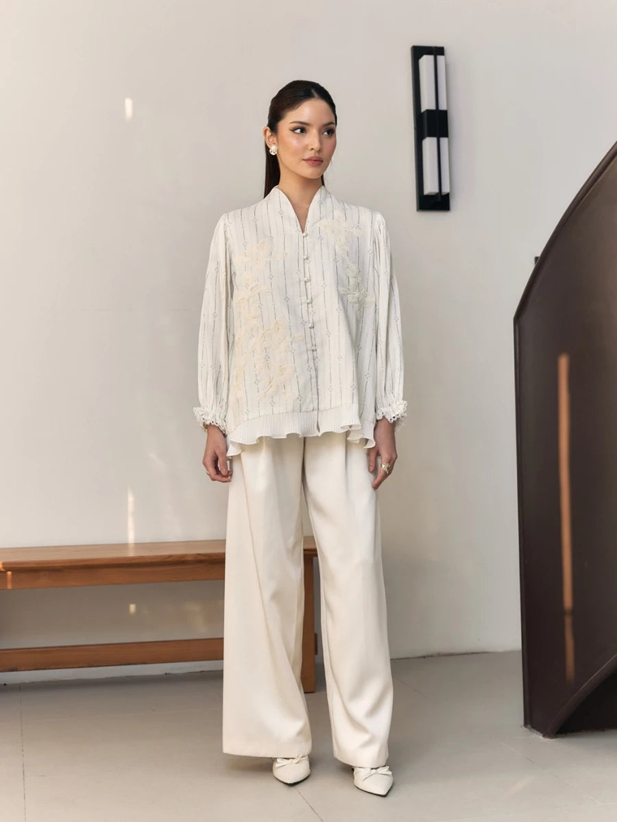 Woman wearing a white embroidered blouse by Studio Tui in a minimal indoor setting