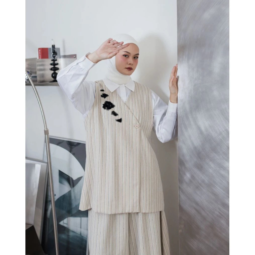 Woman wearing a white hijab, white shirt, and beige pinstripe vest by Maima and pants in an indoor setting.