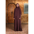 Person wearing a burgundy Mecca Dhurma Abaya by Nehhat Modest in front of a wooden door.