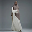 Person wearing a light brown hijab by Nehhat Modest and white abaya on a gray background