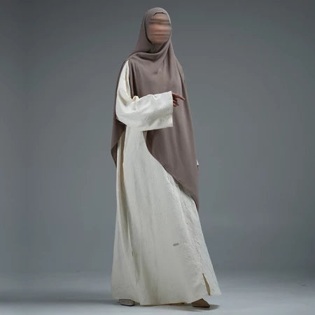 Person wearing a light brown hijab by Nehhat Modest and white abaya on a gray background
