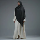 Person wearing a dark grey hijab by Nehhat Modest and white dress on a gray background